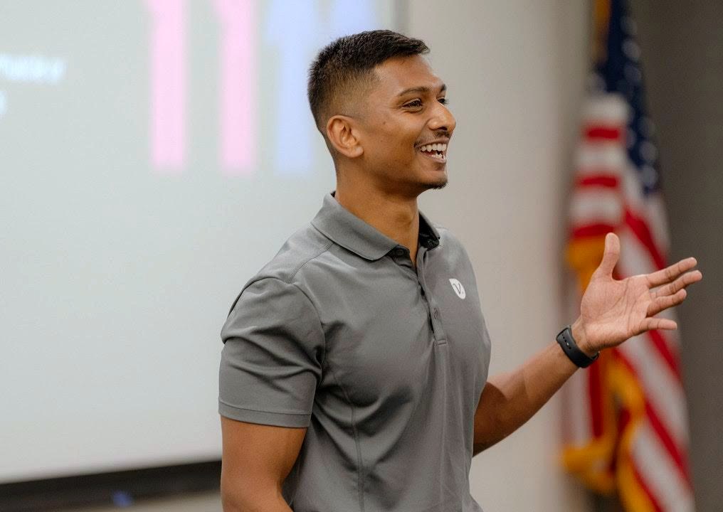 Nicholas Prasad delivering a keynote, American flag in the background